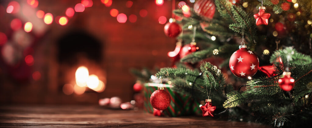 Sapin de Noël avec boules rouges et étoiles devant une cheminée chaleureuse aux lumières festives.