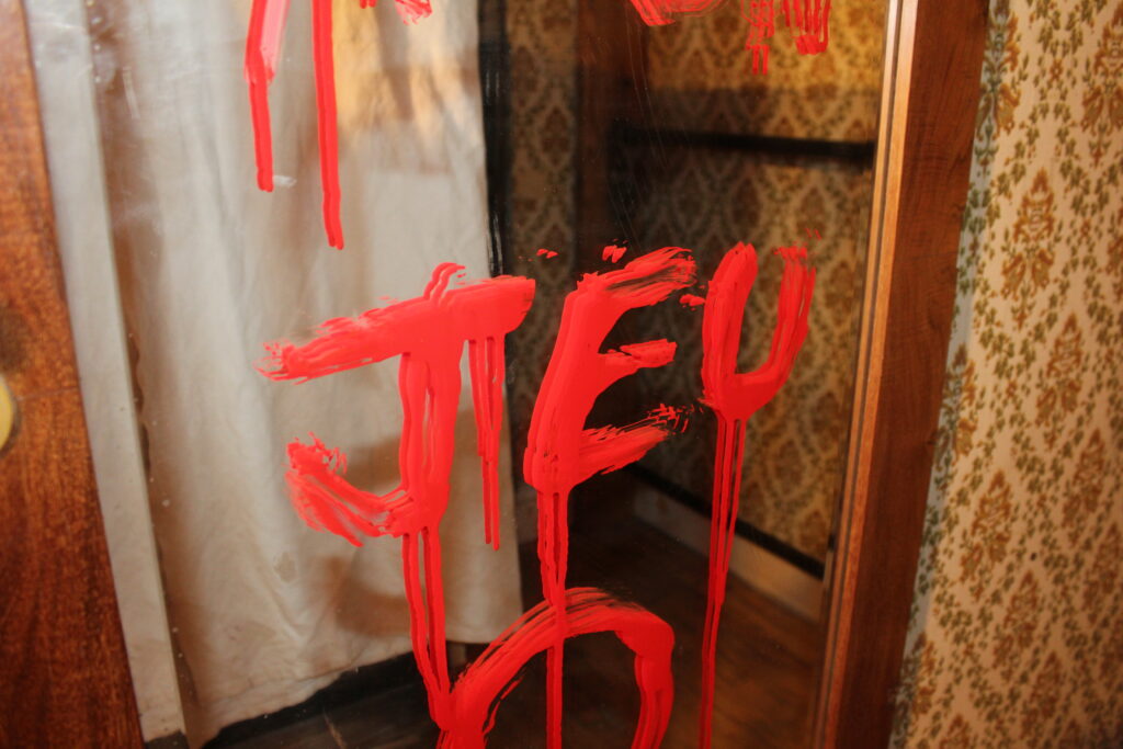 Mot JEU en peinture rouge dégoulinante sur un miroir, décor vintage inquiétant.