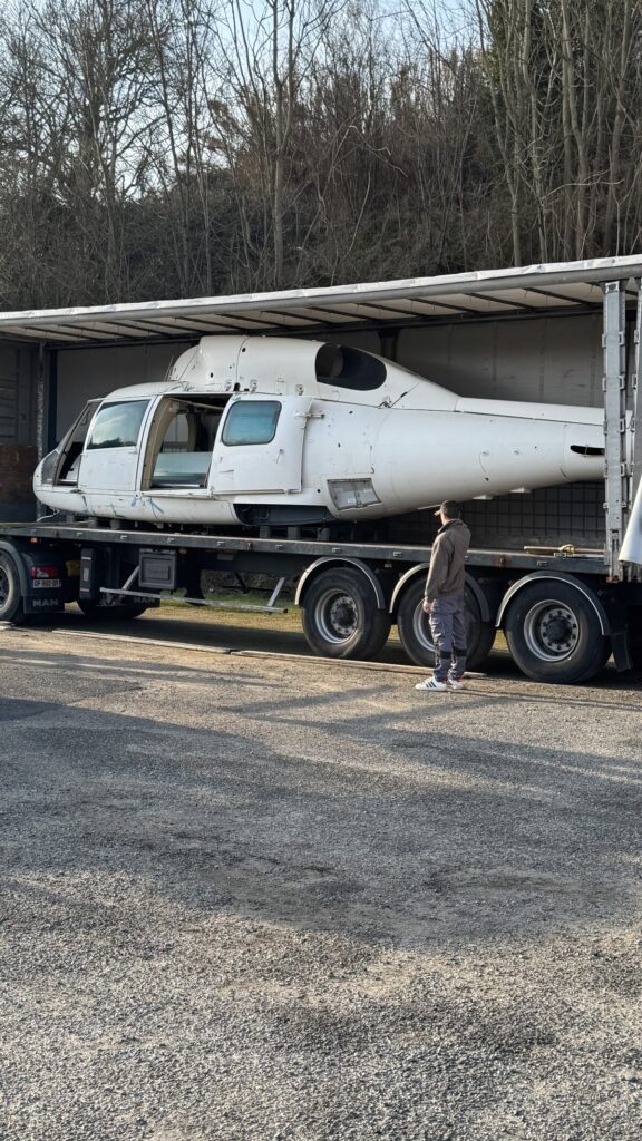 Fuselage d'hélicoptère blanc sur remorque de camion MAN avec un homme à côté.