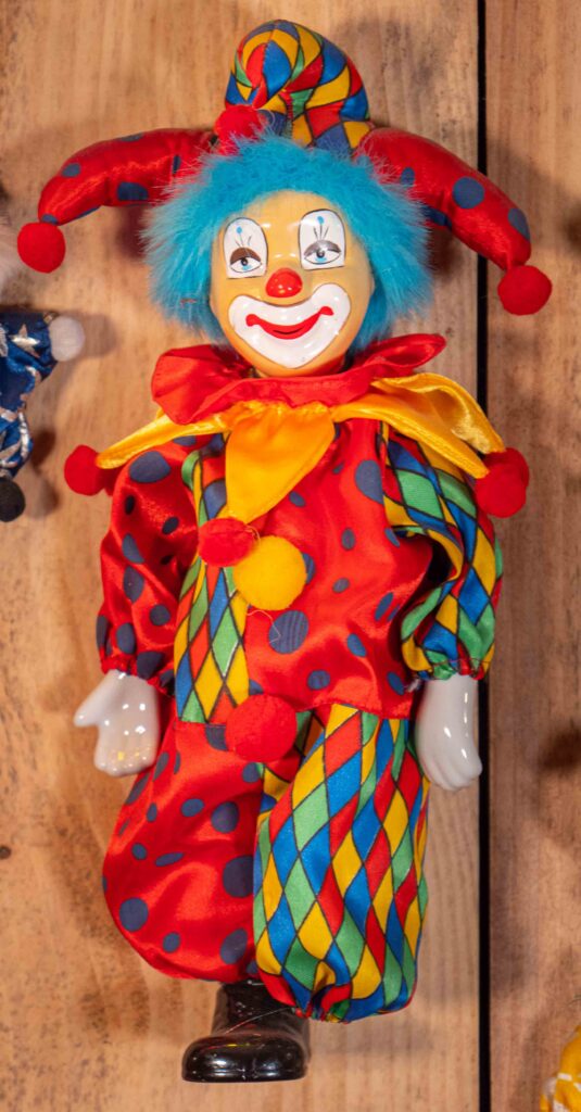 Poupée clown colorée au visage en porcelaine, cheveux bleus et costume arlequin à pois.
